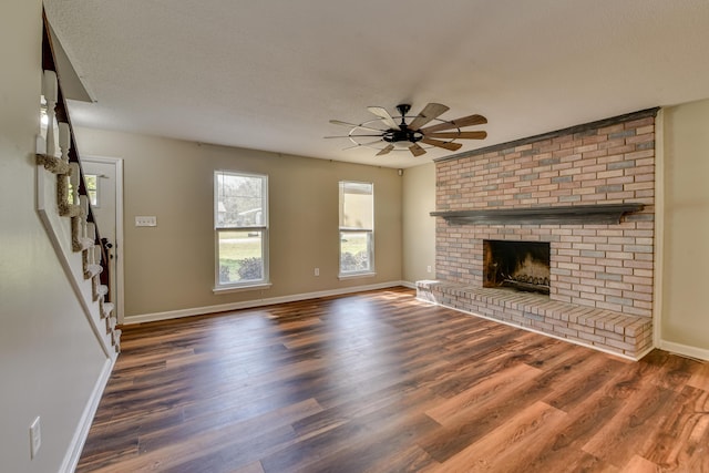 unfurnished living room with a textured ceiling, wood finished floors, a ceiling fan, baseboards, and a brick fireplace