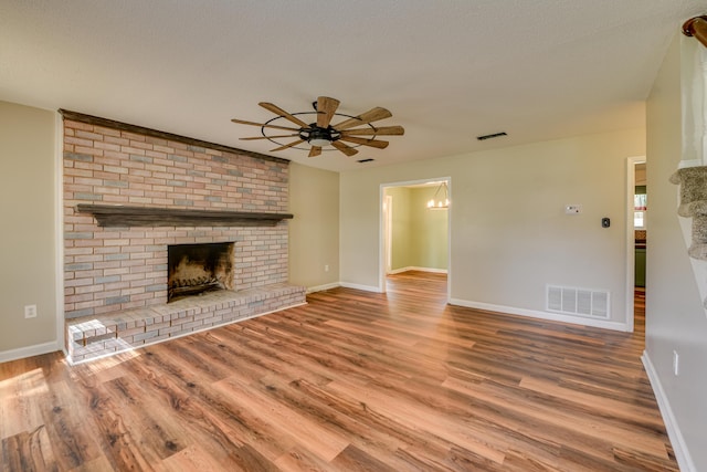 unfurnished living room with ceiling fan, a fireplace, wood finished floors, visible vents, and baseboards