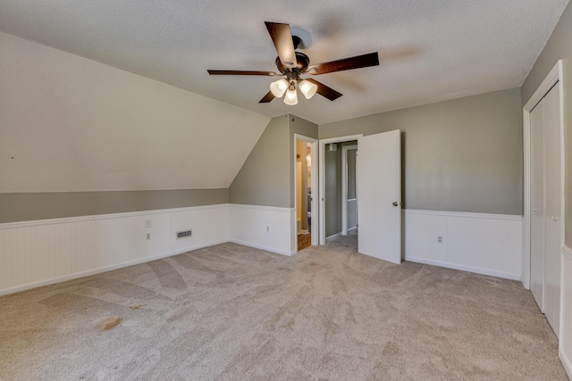 additional living space with a textured ceiling, lofted ceiling, a wainscoted wall, carpet floors, and visible vents