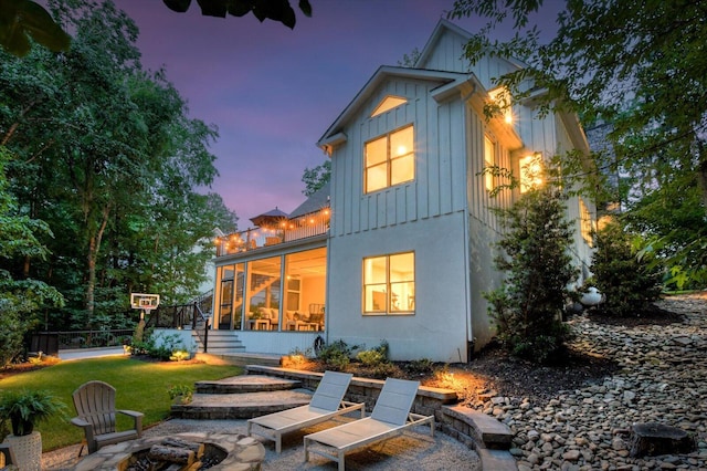 back house at dusk featuring a patio, a fire pit, a lawn, and a sunroom