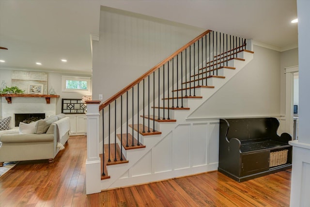 staircase featuring crown molding, a large fireplace, and hardwood / wood-style floors