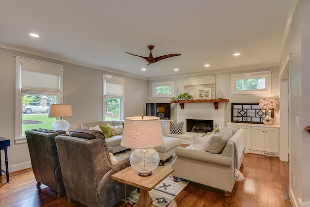 living room with ceiling fan, a large fireplace, wood-type flooring, and ornamental molding