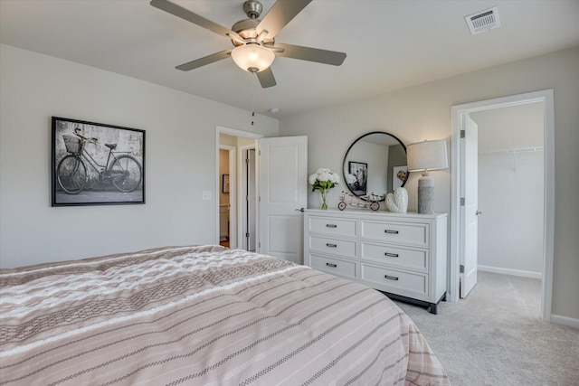 bedroom featuring a spacious closet, a closet, ceiling fan, and light colored carpet