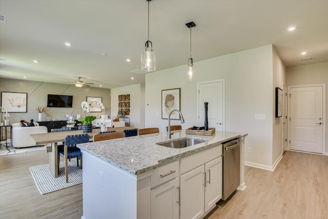 kitchen with white cabinets, a center island with sink, sink, stainless steel dishwasher, and decorative light fixtures