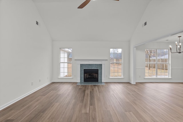 unfurnished living room featuring high vaulted ceiling, hardwood / wood-style floors, a tile fireplace, and a wealth of natural light