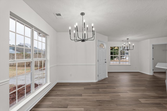 unfurnished dining area featuring an inviting chandelier, dark hardwood / wood-style floors, and a textured ceiling