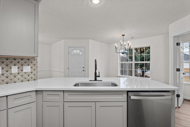 kitchen with gray cabinets, sink, light wood-type flooring, stainless steel dishwasher, and a textured ceiling