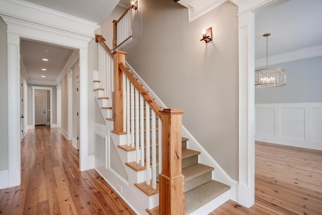 staircase with crown molding, a notable chandelier, visible vents, and hardwood / wood-style flooring