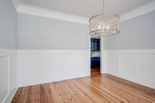 unfurnished dining area featuring ornamental molding, a decorative wall, and a notable chandelier