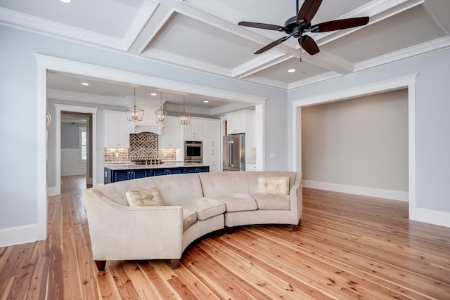 living room featuring crown molding, ceiling fan, light wood-style flooring, baseboards, and coffered ceiling
