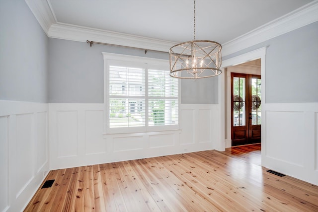 unfurnished dining area featuring light wood finished floors, a decorative wall, a chandelier, a wainscoted wall, and ornamental molding