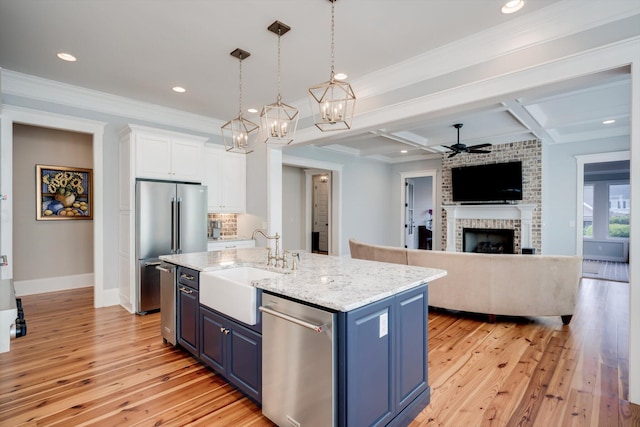 kitchen with ceiling fan with notable chandelier, light wood-style floors, a sink, appliances with stainless steel finishes, and blue cabinetry
