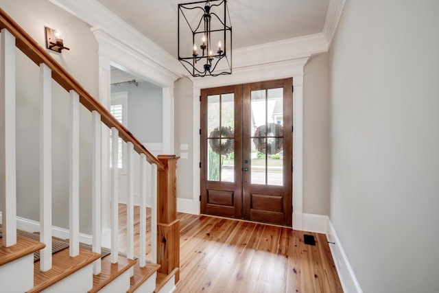 foyer featuring an inviting chandelier, french doors, crown molding, stairway, and light wood-style floors