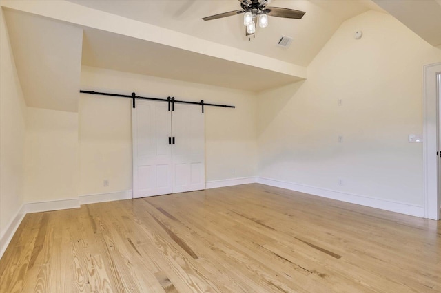 unfurnished room featuring wood-type flooring, a barn door, ceiling fan, and vaulted ceiling