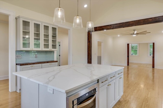 kitchen with pendant lighting, a center island, light stone countertops, white cabinets, and decorative backsplash