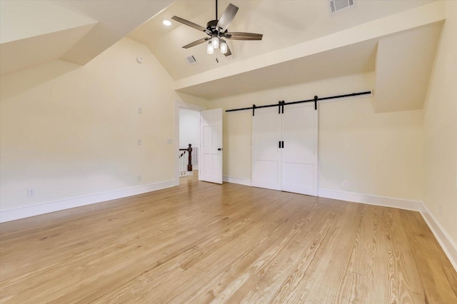 interior space with light hardwood / wood-style flooring, ceiling fan, a barn door, vaulted ceiling, and a closet