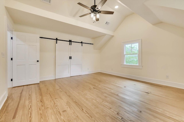 additional living space with ceiling fan, wood-type flooring, a barn door, and vaulted ceiling