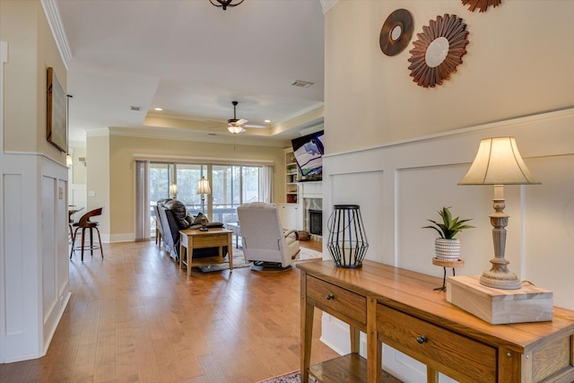 living room with a tray ceiling, crown molding, wood-type flooring, and ceiling fan