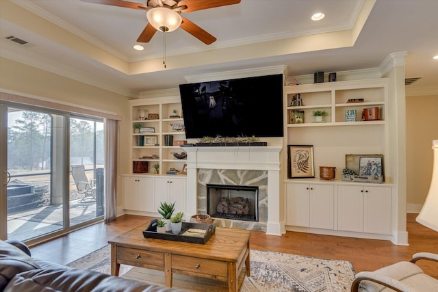 living room featuring ornamental molding, a premium fireplace, a raised ceiling, and light hardwood / wood-style flooring