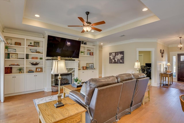 living room featuring ceiling fan, a fireplace, a tray ceiling, and light hardwood / wood-style floors