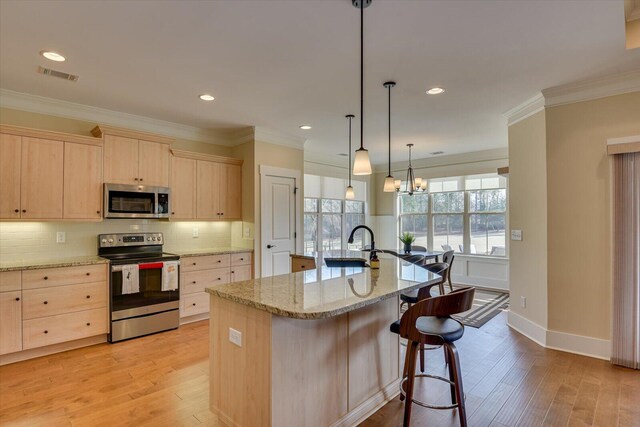 kitchen with light wood-type flooring, light brown cabinets, appliances with stainless steel finishes, a kitchen island with sink, and backsplash