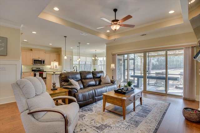 living room with ornamental molding, a raised ceiling, ceiling fan with notable chandelier, and light hardwood / wood-style flooring