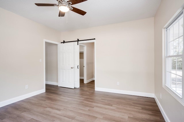 empty room featuring ceiling fan, a wealth of natural light, light hardwood / wood-style flooring, and a barn door