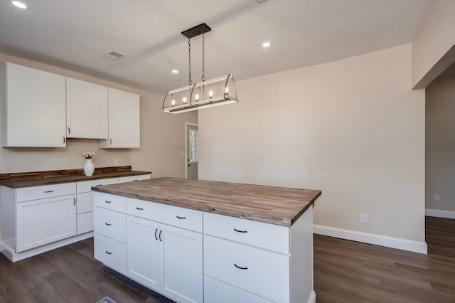 kitchen featuring a center island, hanging light fixtures, a textured ceiling, white cabinets, and butcher block counters