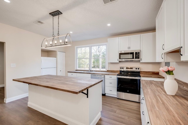 kitchen with appliances with stainless steel finishes, a center island, wooden counters, decorative light fixtures, and white cabinetry