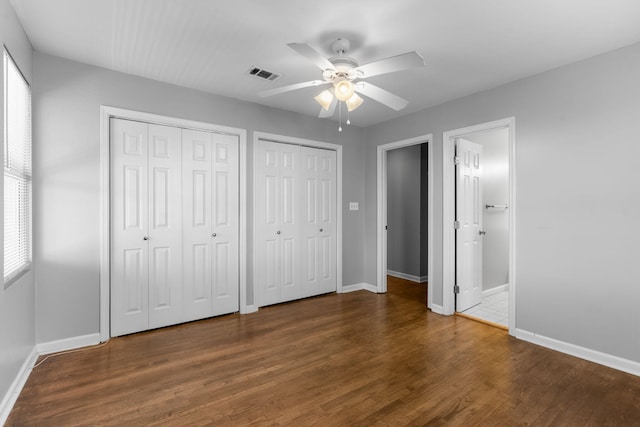 unfurnished bedroom featuring multiple windows, ceiling fan, two closets, and dark hardwood / wood-style floors