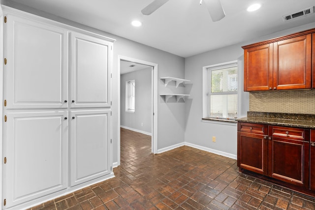 kitchen featuring decorative backsplash, ceiling fan, and dark stone counters