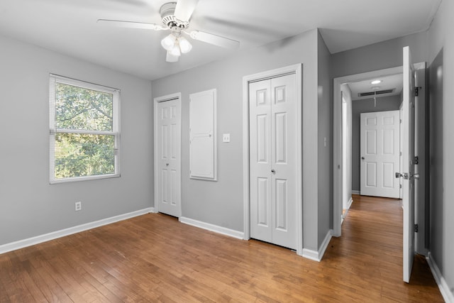 unfurnished bedroom featuring ceiling fan, light wood-type flooring, and two closets