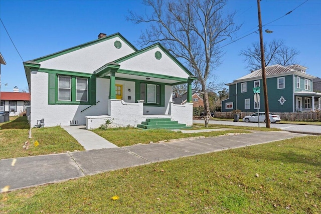 bungalow-style home featuring a front yard, covered porch, a chimney, and stucco siding