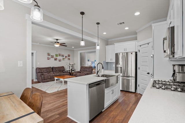 kitchen with sink, a kitchen island with sink, stainless steel appliances, white cabinets, and decorative light fixtures