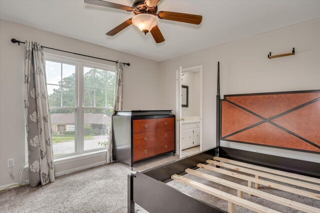 bedroom with connected bathroom, light colored carpet, multiple windows, and ceiling fan