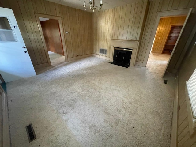 unfurnished living room featuring a chandelier, light carpet, a large fireplace, and wooden walls