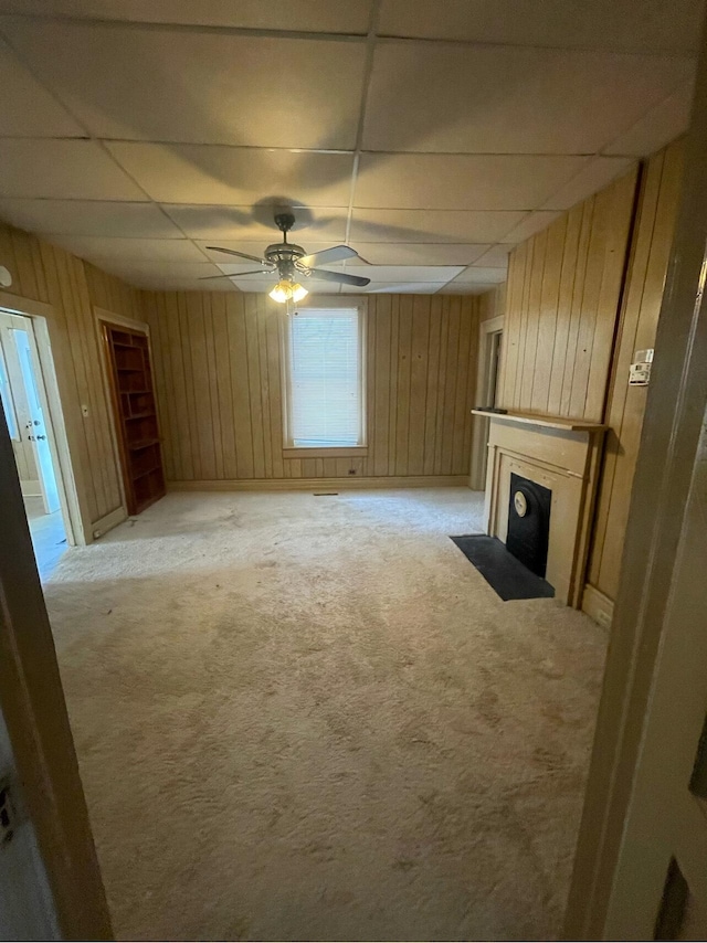 unfurnished living room featuring ceiling fan, a drop ceiling, light carpet, and wooden walls