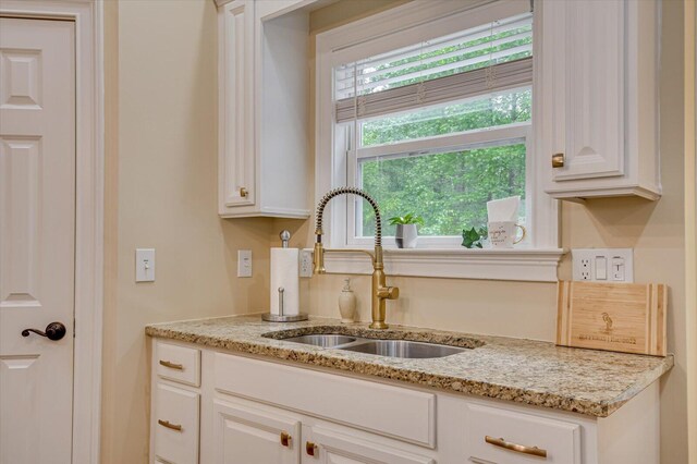 kitchen featuring white cabinets, light stone counters, and sink