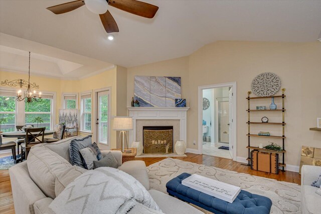 living room featuring ceiling fan with notable chandelier, light hardwood / wood-style flooring, and vaulted ceiling