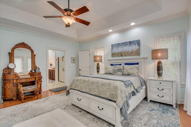 bedroom with ceiling fan, a raised ceiling, light wood-type flooring, and ensuite bath