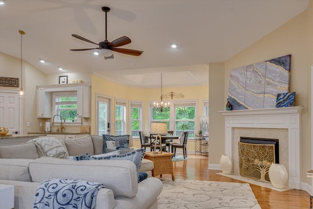 living room with lofted ceiling, light hardwood / wood-style flooring, ceiling fan with notable chandelier, and sink