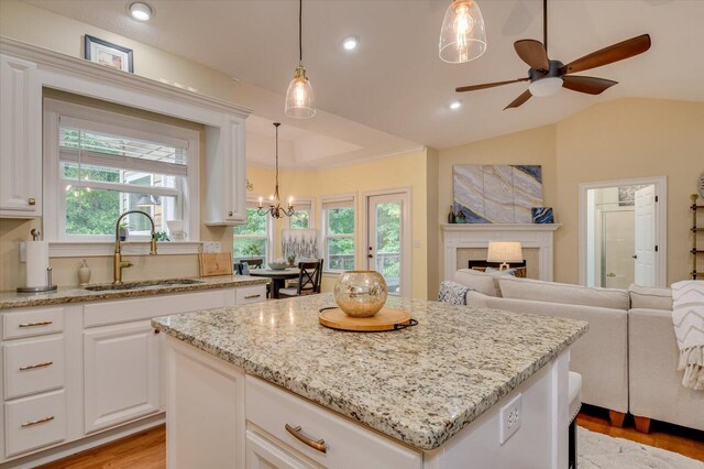 kitchen featuring ceiling fan with notable chandelier, a kitchen island, sink, white cabinetry, and lofted ceiling