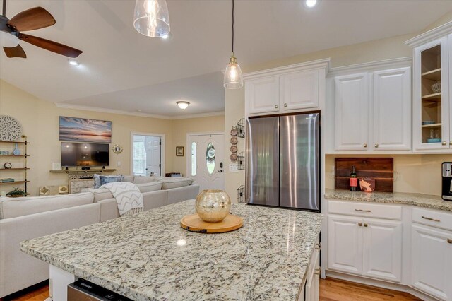 kitchen featuring stainless steel refrigerator, white cabinetry, ceiling fan, hanging light fixtures, and light stone counters