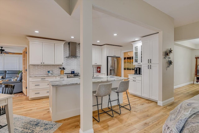 kitchen featuring appliances with stainless steel finishes, light wood-type flooring, wall chimney exhaust hood, tasteful backsplash, and an island with sink