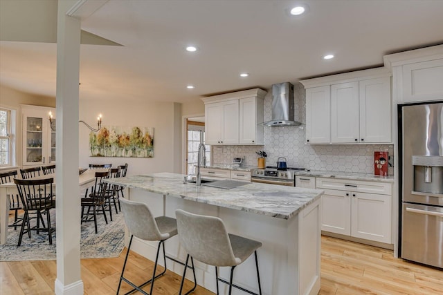 kitchen with stainless steel appliances, light wood-type flooring, wall chimney range hood, and decorative backsplash