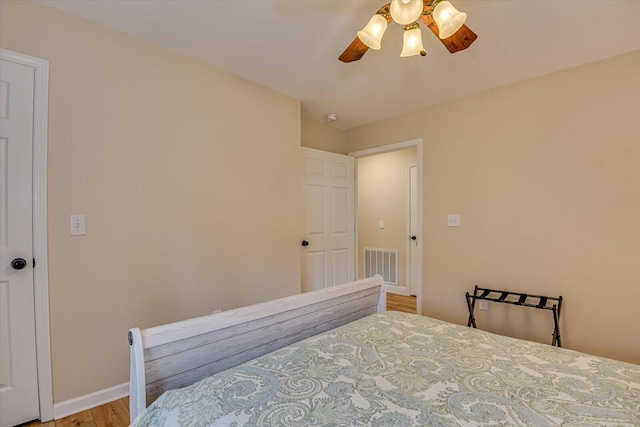 bedroom with a ceiling fan, visible vents, baseboards, and wood finished floors