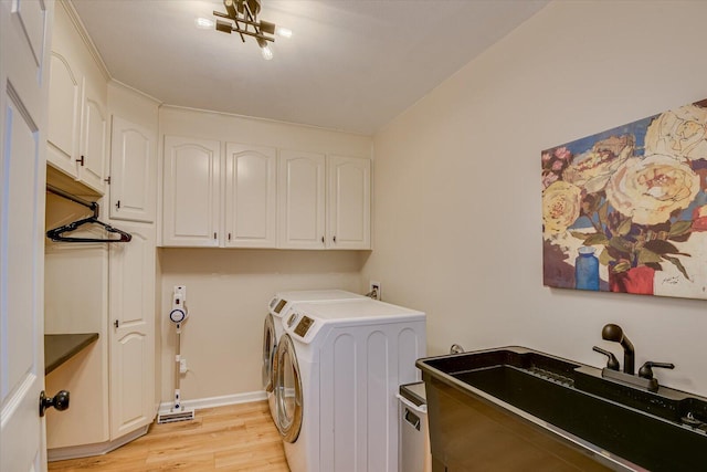 washroom featuring a sink, baseboards, washer and dryer, cabinet space, and light wood finished floors