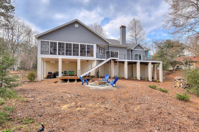 back of house featuring a deck, a fire pit, a sunroom, stairway, and a chimney