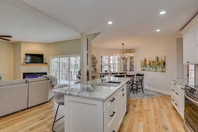 kitchen with appliances with stainless steel finishes, open floor plan, light wood-style floors, a kitchen bar, and a sink