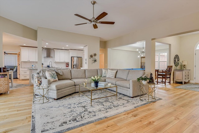 living room with ceiling fan with notable chandelier, light wood finished floors, baseboards, and recessed lighting